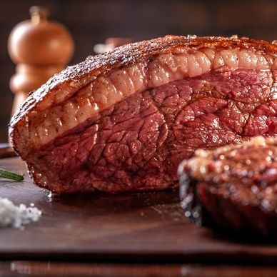 Sliced grilled picanha with a crisp, golden-brown fat cap resting on a wooden cutting board atop a k