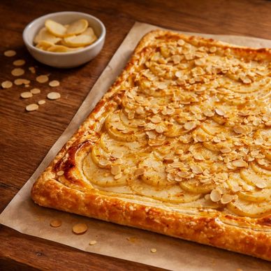 White wine poached pear and goat cheese puff pastry tart topped with sliced almonds on a rustic wood