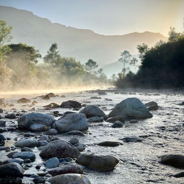 A rocky riverbed with mist and mountains in the background.