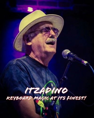 Musician Itzadino passionately performs keyboard magic on stage wearing a hat and sunglasses.