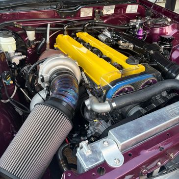 Close-up of a car engine with a yellow valve cover and large air intake.