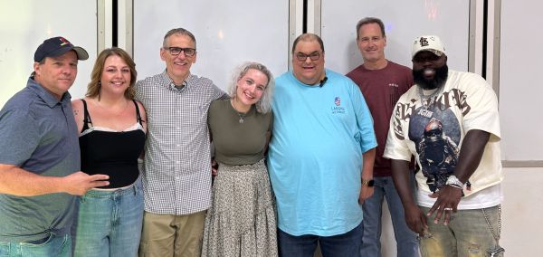 A group of seven diverse adults smiling and posing together indoors.