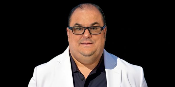 Man wearing glasses and a white blazer against a black background.