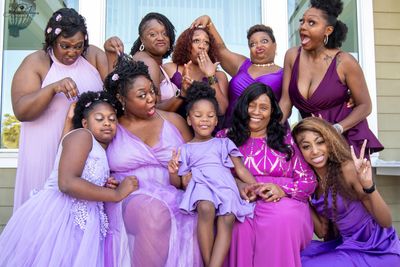 Group of joyful women and girls in purple dresses posing playfully.