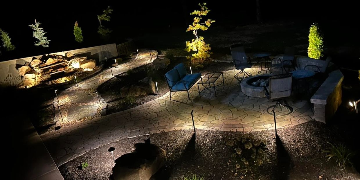 night setting of a backyard with landscaping outdoor lighting, waterfall, and firepit.