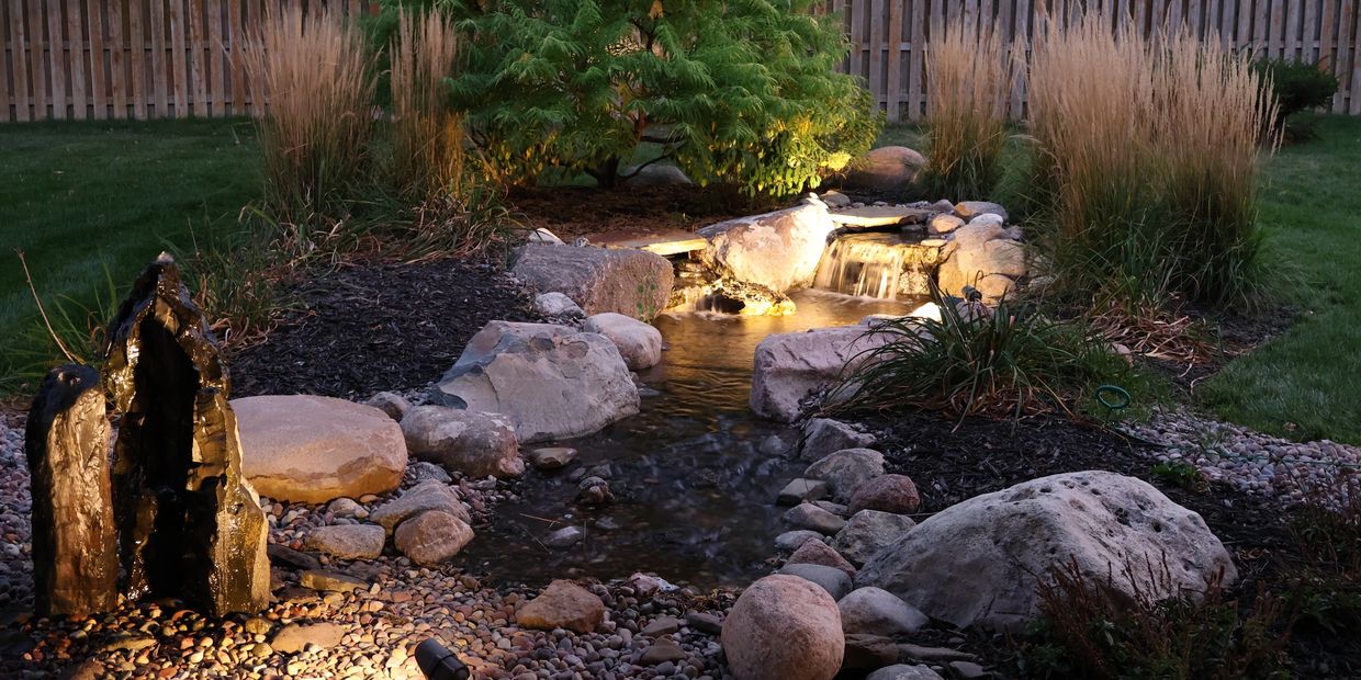Outdoor lighting featuring a residential backyard waterfall and rocks.