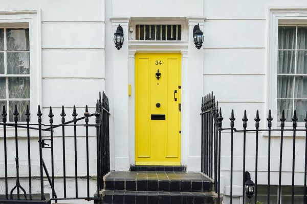 Bright yellow door on a white house with black railings and steps.