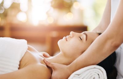 woman laying on a massage table covered in a sheet receiving massage on the neck and shoulders.