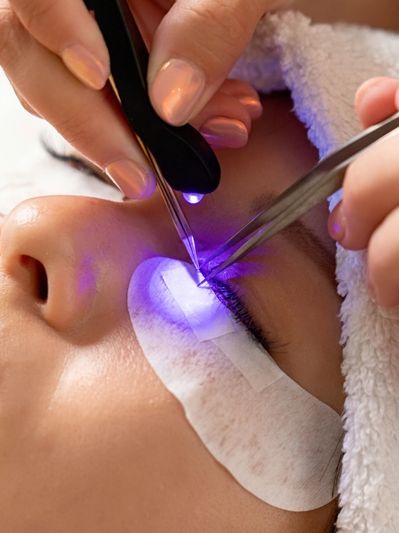 Close-up of eyelash extension application with tweezers and blue light.
