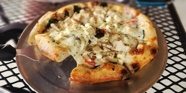 A cheesy chicken pizza slice being lifted from a metal tray.