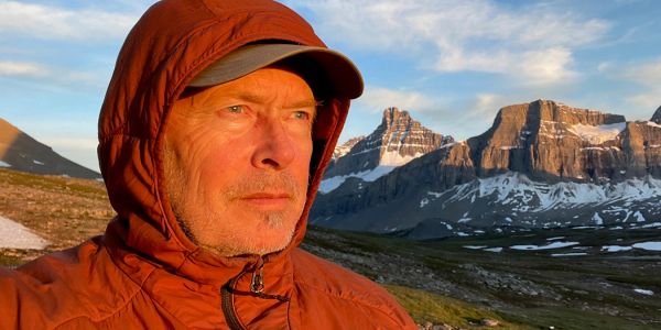 Man in orange jacket enjoys mountain sunrise.