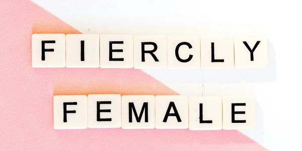Scrabble tiles spell out 'Fiercly Female' on a pink and white background.
