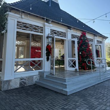 A white pavilion decorated with Christmas wreaths and a large Christmas tree outside.