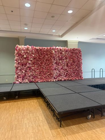 A stage with a large pink flower wall backdrop in an indoor venue.