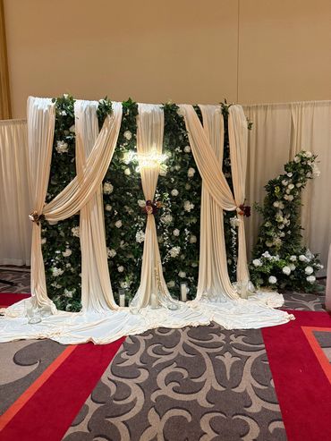 Elegant floral backdrop with white drapes and greenery for an event.