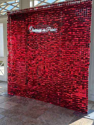 Red sequin wall with "Christmas on Pointe" neon sign in a bright indoor space.
