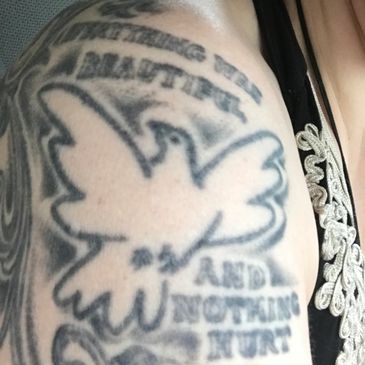 Tattoo of a dove with text on an arm.