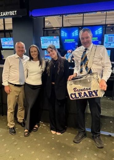 Four people posing in front of betting screens, one holding a personalized sign.