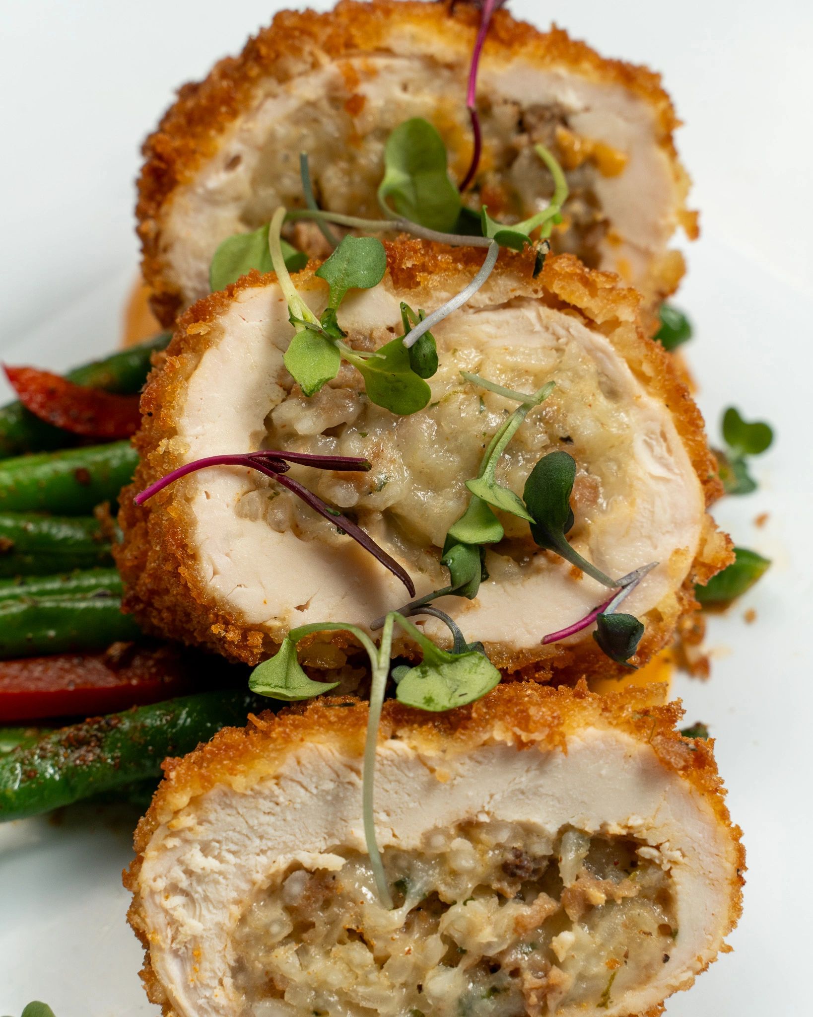 Sliced breaded chicken stuffed with creamy filling and garnished with microgreens.