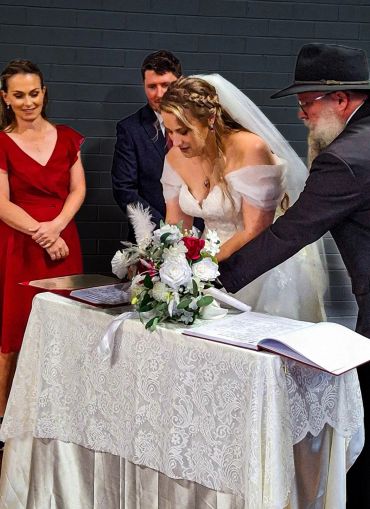 Bride signing wedding documents with groom and guests.