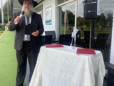 Man in formal attire speaking at an outdoor event.