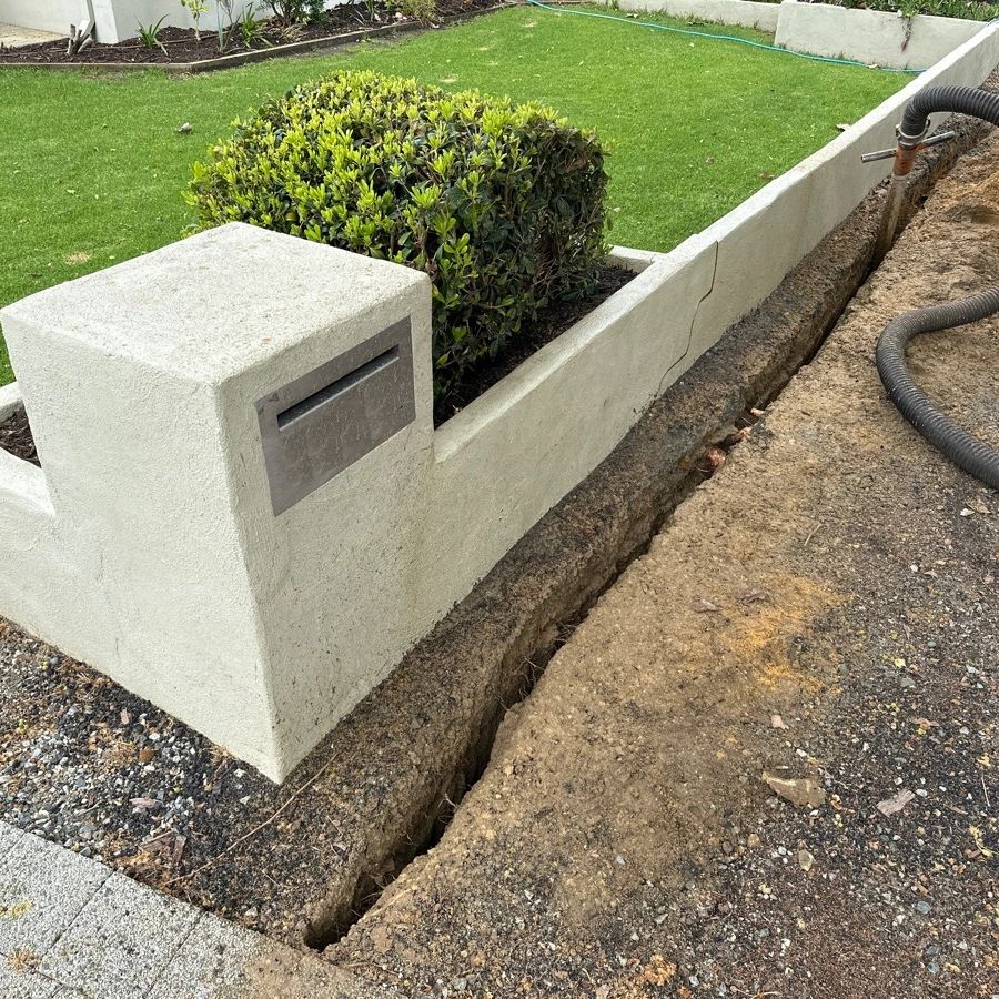 A trench dug beside a concrete planter with a mailbox slot.