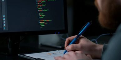 Person working on coding and writing notes with Satwise logo visible on screen and paper.