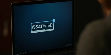 Person using a laptop displaying the SATWISE logo on screen.