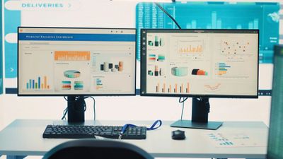 Dual monitors display financial data and graphs on a clean desk setup.