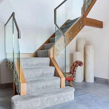 Glass stair case with wooden hand rail and grey carpet 