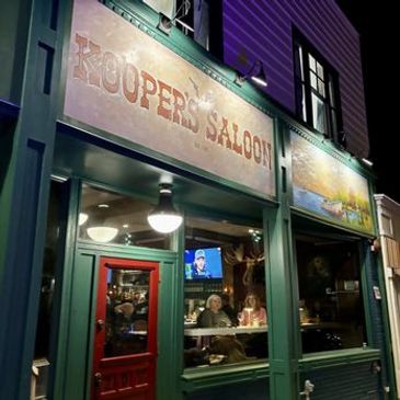 Exterior of Koopers Saloon at night with patrons inside.