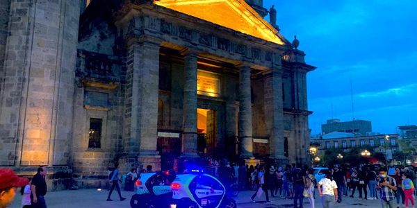 Edificio antiguo iluminado con policía y gente alrededor al anochecer.