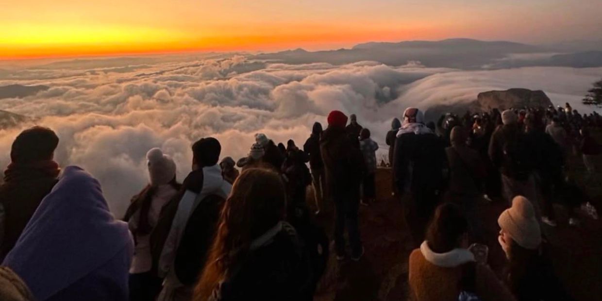 Personas observando un amanecer sobre un mar de nubes.