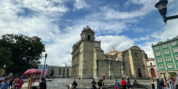 Edificio histórico y plaza con personas bajo un cielo parcialmente nublado.