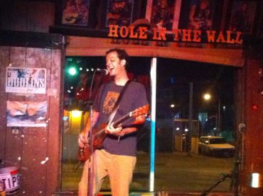 Musician playing guitar and singing at Hole in the Wall venue.