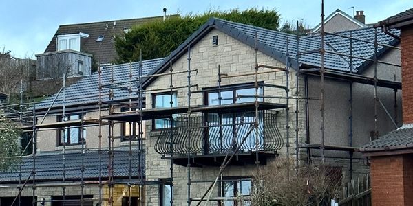 House under renovation with scaffolding and a white fence on a sloped driveway.