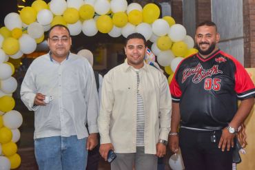 Three men posing with yellow and white balloons.