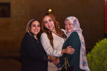 Three women smiling and posing together at night.