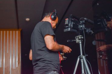 Man operating a video camera with headphones on.