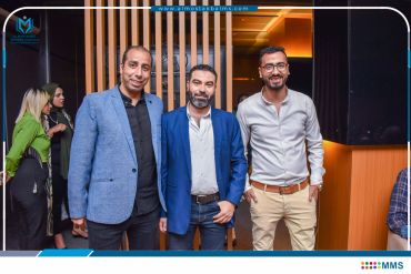 Three men posing together indoors, two in blazers, one in casual attire.