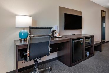 Modern hotel room workspace with desk, chair, lamp, TV, mini fridge, and microwave.