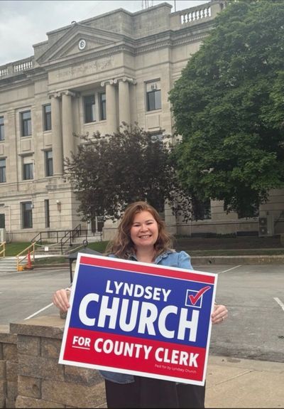 Woman holding a campaign sign for Lyndsey Church for County Clerk.