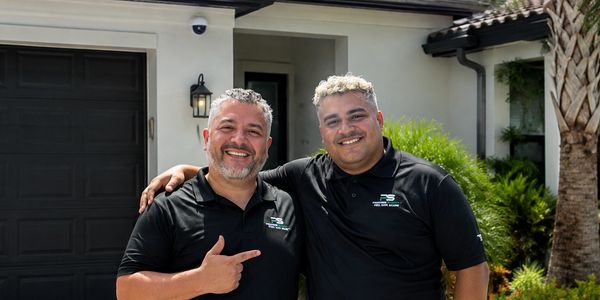 Two men smiling in front of a house.