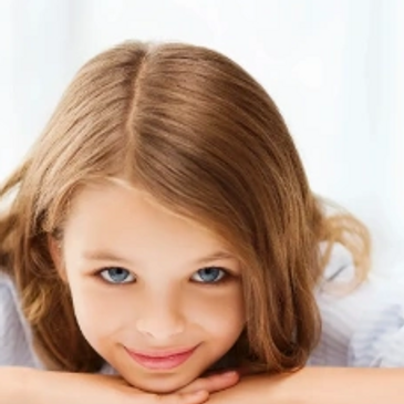 Smiling young girl with blue eyes resting her chin on her hands.