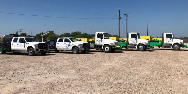 Fleet of work trucks in a dusty lot under clear blue sky.