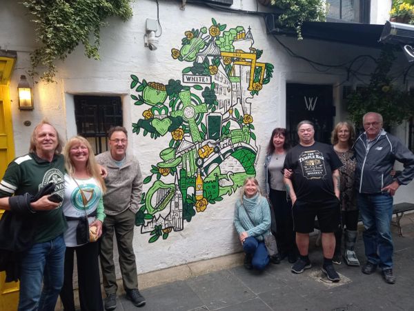 Group of people posing by a colorful mural on a white wall.