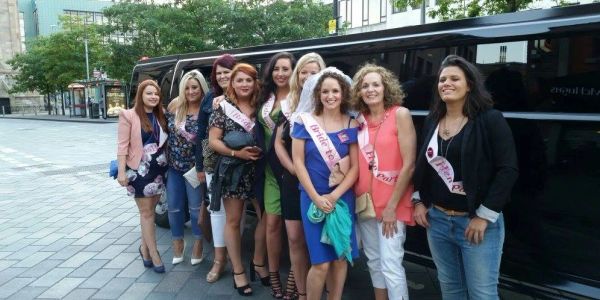 Group of women with sashes standing in front of a limousine.