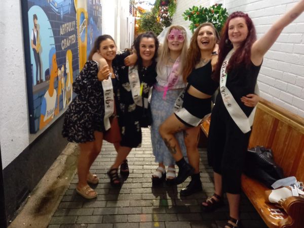 Group of five smiling women in festive sashes.