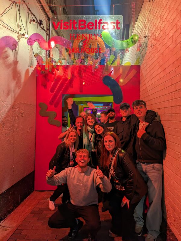 Group of friends posing at vibrant Visit Belfast Henry's Jailhouse entrance.