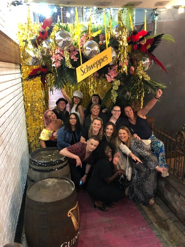 Group of friends posing under a decorated Schweppes sign.